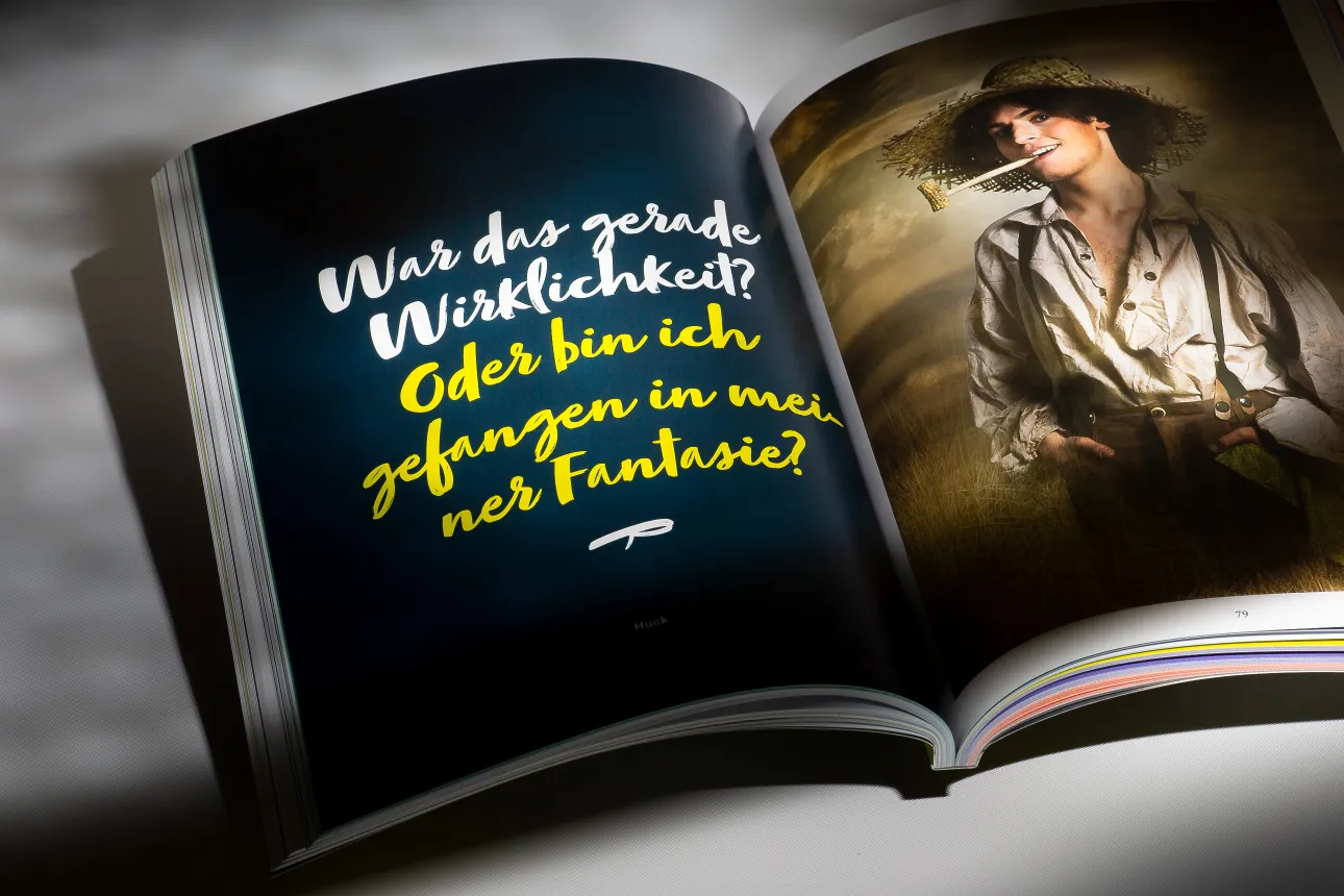 Aufgeschlagenes teatro-Programmheft mit Zitat „War das gerade Wirklichkeit?“ und Porträt von Huck mit Strohhut